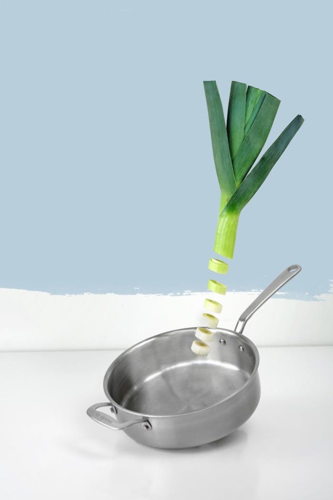 Artistic presentation of a sliced leek over a stainless steel pan against a clean, blue background.