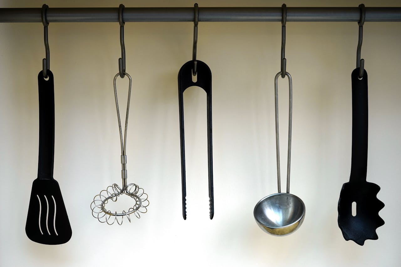 Services A set of stainless steel and plastic kitchen utensils hanging on a rail.