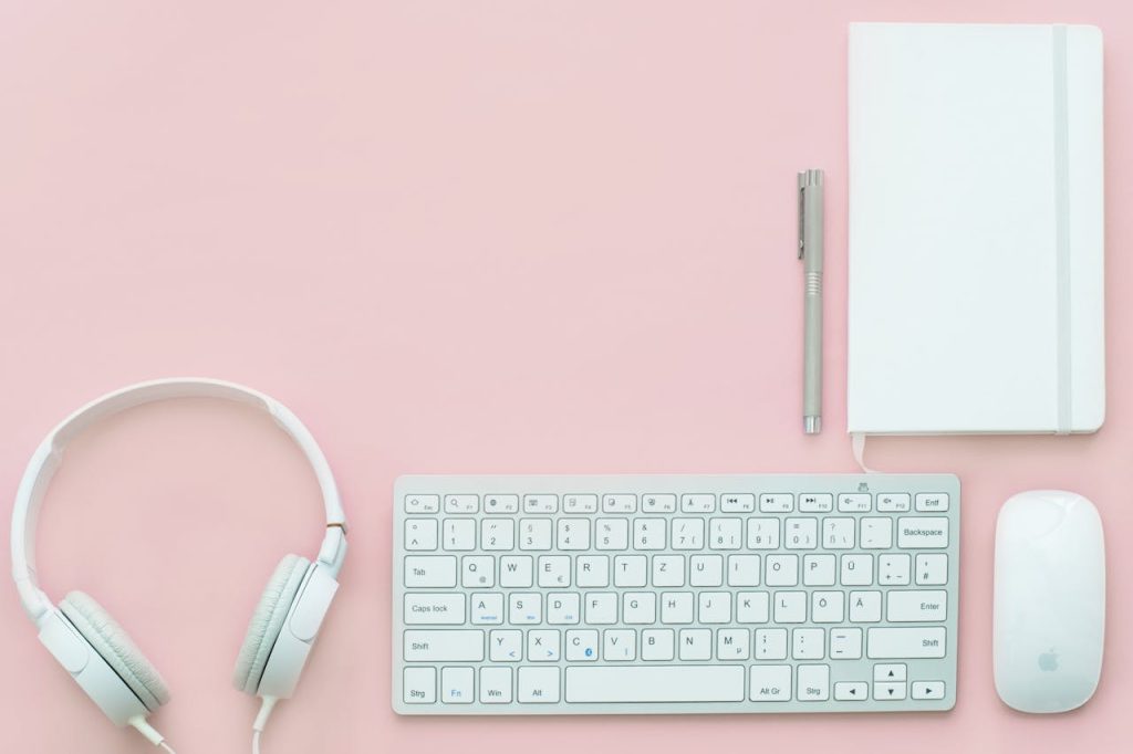 Elegant flat lay of white electronics and stationery on pastel pink background.